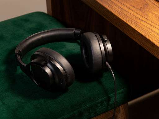 Close-up van matzwarte podcastkoptelefoon op groene fluwelen achtergrond met warm licht.